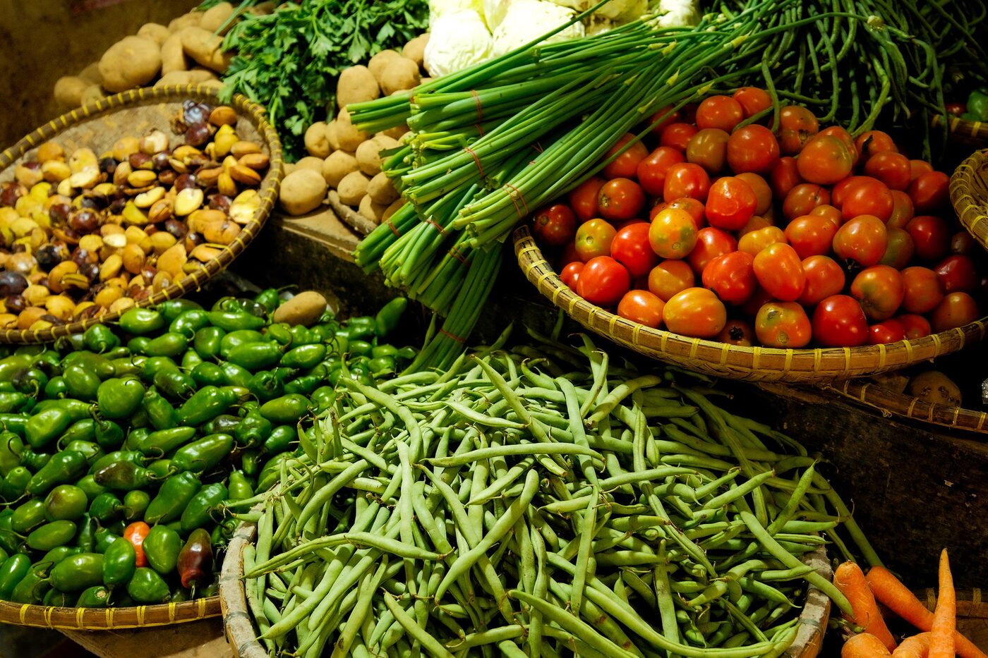 Market baskets heaped with green beans, chillies, tomatoes, maize and herbs.
