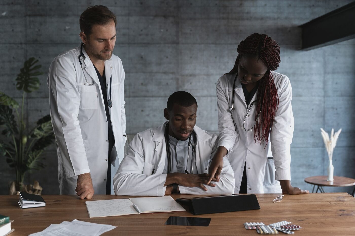 Three clinicians in white coats gathered around a desk, reviewing notes together.